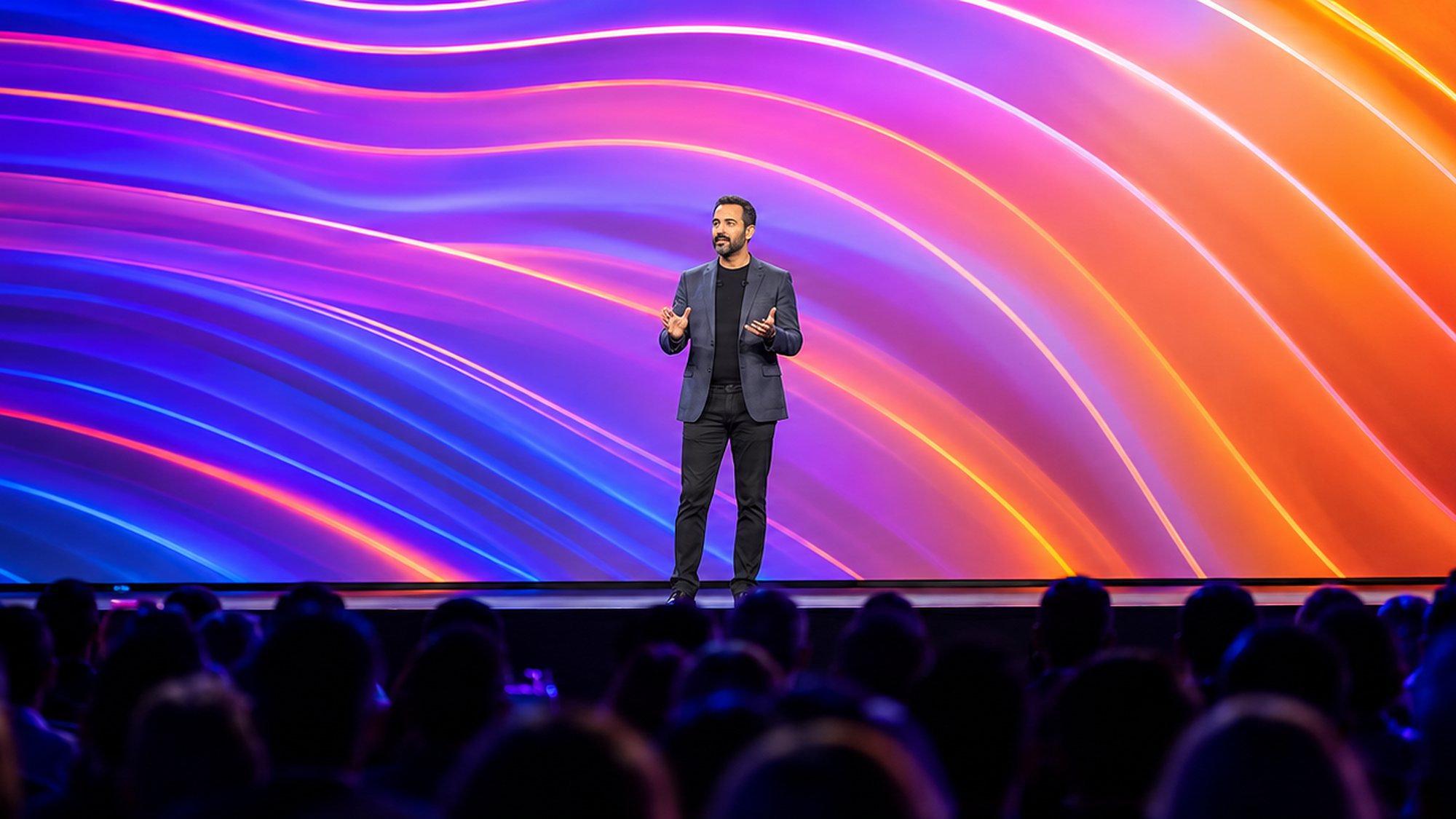 A speaker on stage in front of a large light wall, a frame from an event film